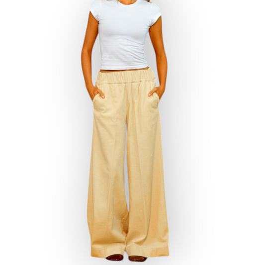 Model wearing Ygreque Sea Me Happy ecru organic cotton corduroy wide-leg trousers against a textured yellow wall