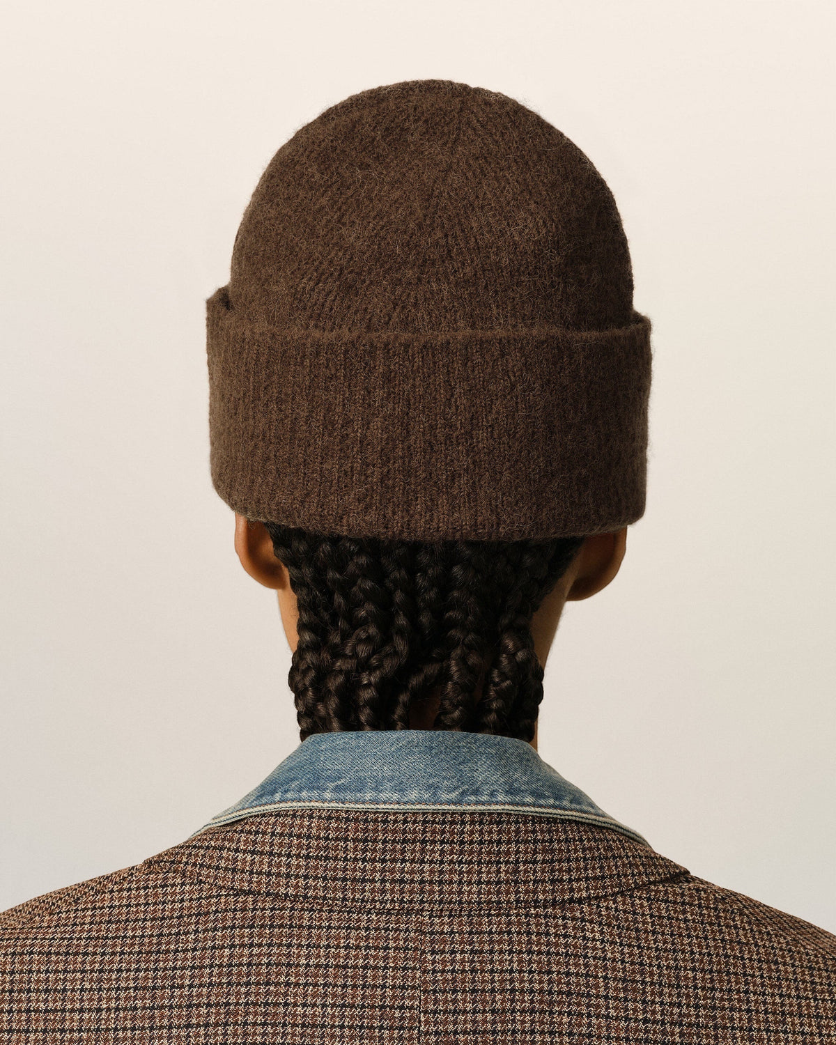 Back view of a person wearing a brown Ami Paris alpaca beanie in interlock knit, styled with a plaid blazer.
