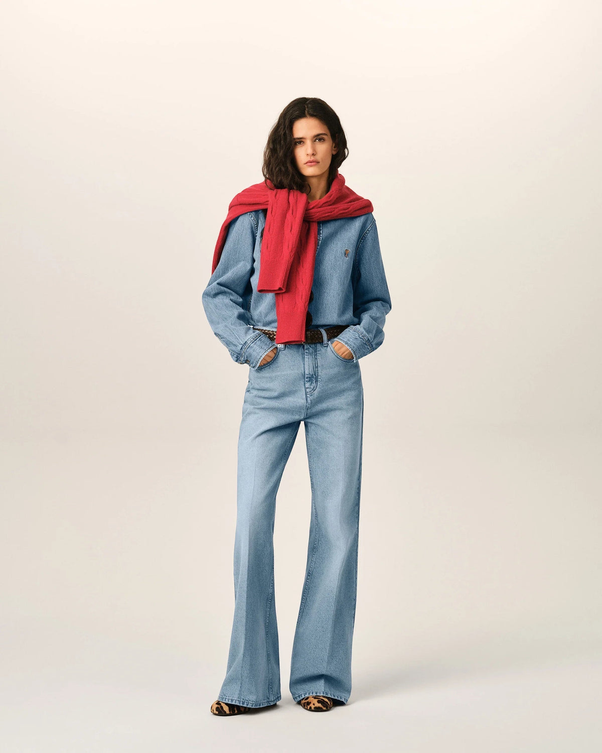 Model wearing Ygreque Ami Paris light blue denim shirt with tobacco embroidery and red sweater draped over shoulders